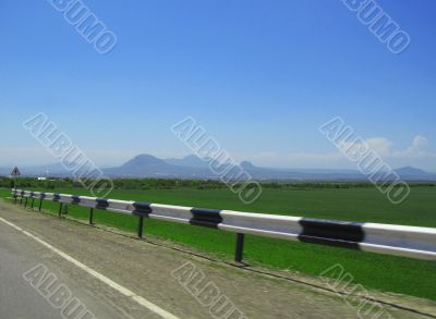 Wide highway and mountain. Clouds over and blue sky Wide highway and mountain. Clouds over and blue sky
