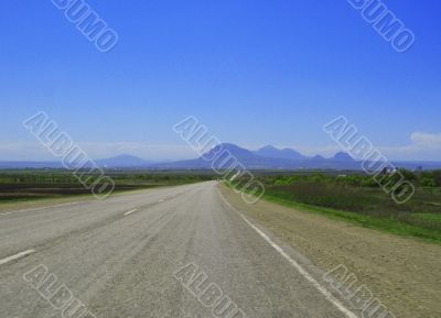 Wide highway and mountain. Clouds over and blue sky