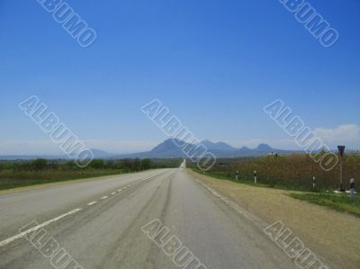 Wide highway and mountain. Clouds over and blue sky