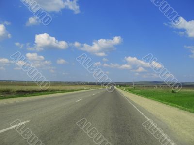 Wide highway and meadow. Clouds over and blue sky