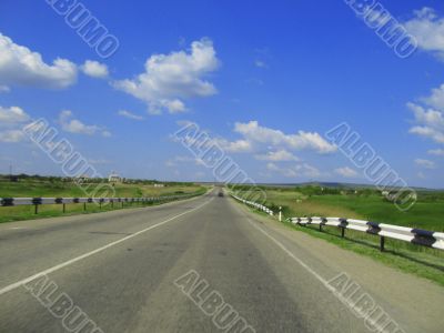 Wide highway and meadow. Clouds over and blue sky