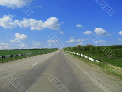 Wide highway and meadow. Clouds over and blue sky