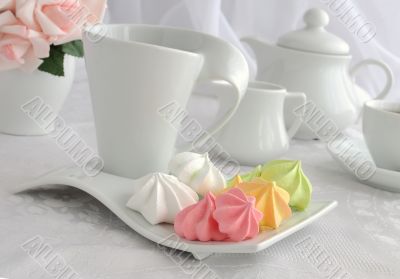 Meringue cookies of different colors on a plate with a cup of co