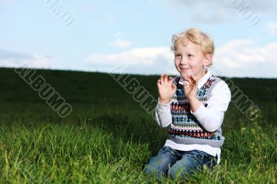 Impish little boy kneeling in green field