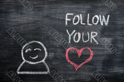 Speech bubble with a cartoon figure and the phrase `Follow your heart` drawn on a blackboard background