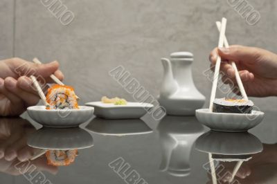 hands holding sushi with chopsticks at restaurant