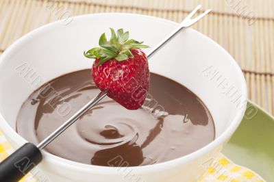 strawberry on fondue stick and melted chocolate bowl