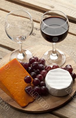 view of a wooden board with wine glass grapes and cheese