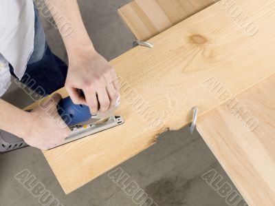 overhead image of a man cutting sheet of a wooden plank