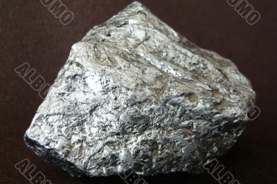 Silvery shiny stone on a dark brown background.