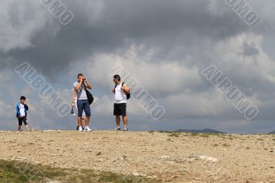 Several people are on top of the mountain against the dark clouds. 