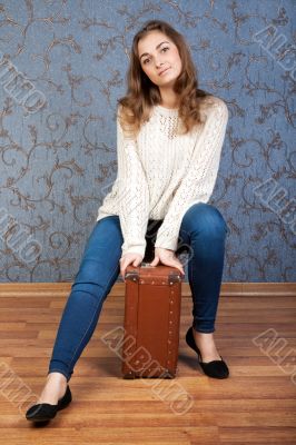 Beautiful young girl sitting on an old brown suitcase in the int