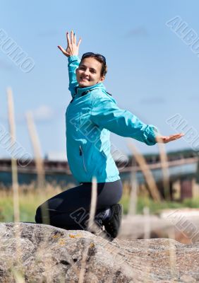 Beautiful girl in a jacket kneeling on a rock