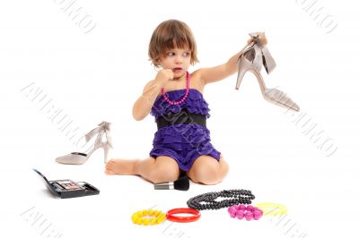 Cute little girl with cosmetics and women`s shoes in the studio