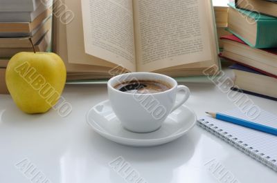 A cup of coffee and an apple on a table among books
