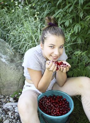 Cheerful girl sitting with a bucket of cherries