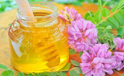 glass jar full of honey and stick with acacia pink and white flo