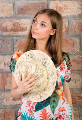 Portrait of pensive girl with a straw hat in hand.