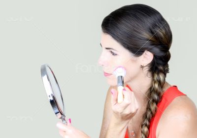 Attractive young woman looking at the mirror, applying make up