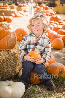 Little Boy Sitting and Holding His Pumpkin at Pumpkin Patch