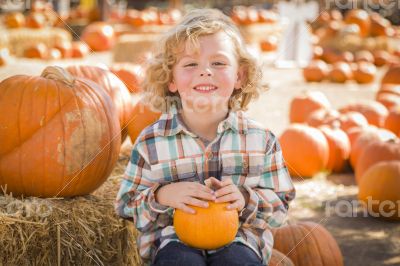 Little Boy Sitting and Holding His Pumpkin at Pumpkin Patch