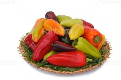 Red, yellow and green peppers on the wicker dish on a white back
