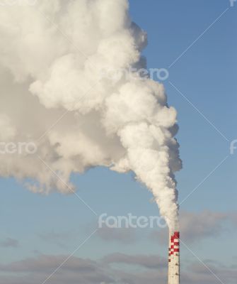 Smokestacks with white steam in the blue sky.