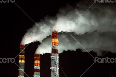 Factory pipes with white steam against the night black sky.