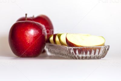 Two ripe red apples and segments of apple on a plate