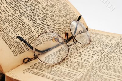 The opened old dictionary with glasses