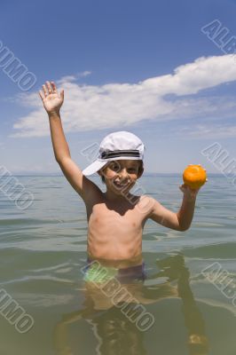 The boy with an orange on a background of the sea