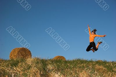 Woman jumping in a hay bales field