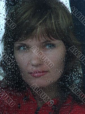 Girl looks thru waterdropped widow glass