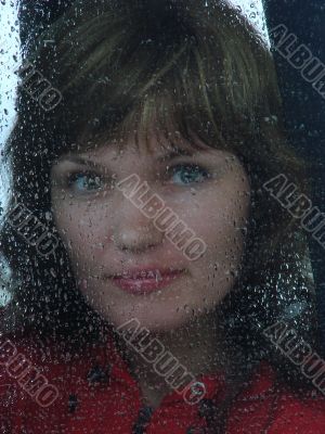 Girl looks thru waterdropped widow glass