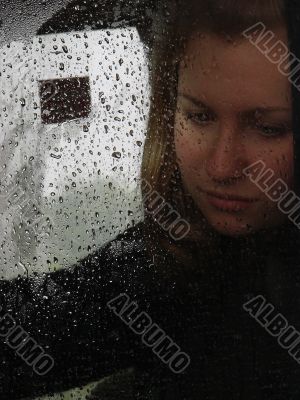 Girl looks thru waterdropped widow glass