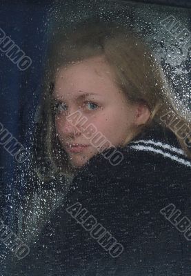 Girl looks thru waterdropped widow glass