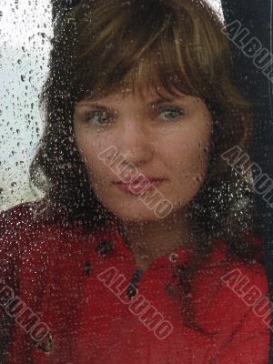 Girl looks thru waterdropped widow glass