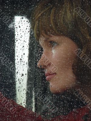 Girl looks thru waterdropped widow glass