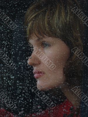 Girl looks thru waterdropped widow glass