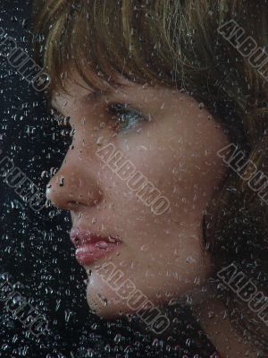 Girl looks thru waterdropped widow glass