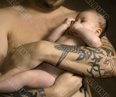The baby on hands at the man with a tattoo