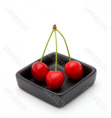 Three cherries in a black bowl