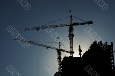 Cranes on high building in front of the sun
