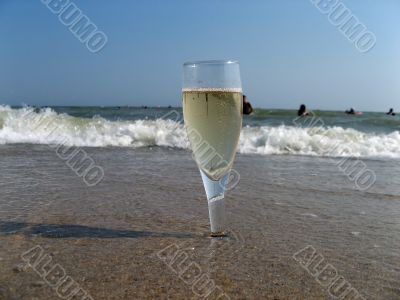 Glass of a cold champagne in warm sea waves