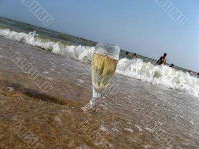 Glass of a cold champagne in warm sea waves