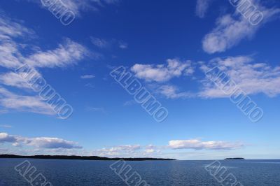 Blue sky with clouds above blue lake
