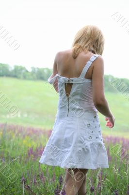 Girl in white dress going away on meadow