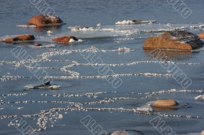 Stones and Ice Patterns in Snow on Seaside in Sunny Day