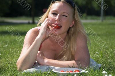 Blond woman eating a strawberry in the park