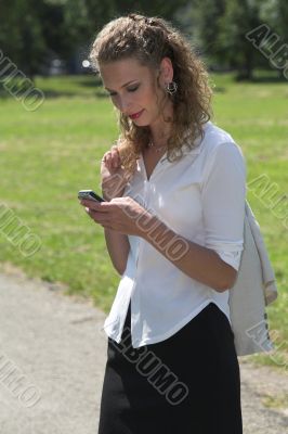 Businesswoman in the park sending a text message